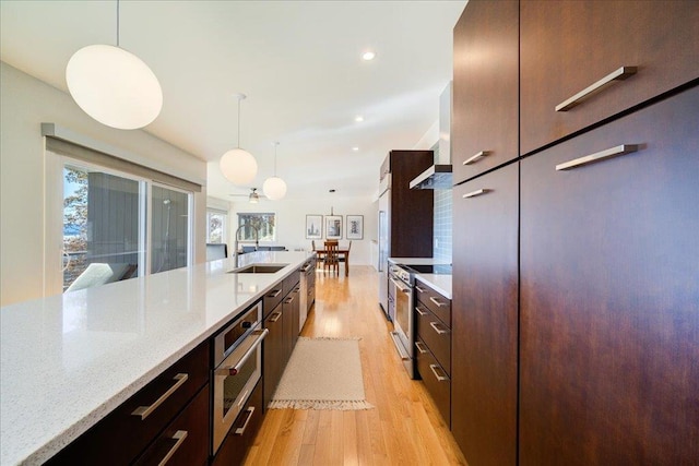 kitchen featuring light stone countertops, sink, light hardwood / wood-style floors, pendant lighting, and appliances with stainless steel finishes