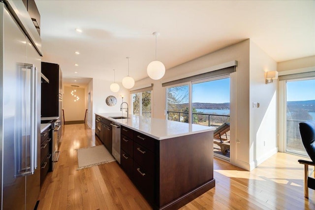 kitchen with a center island with sink, pendant lighting, light wood-type flooring, and appliances with stainless steel finishes