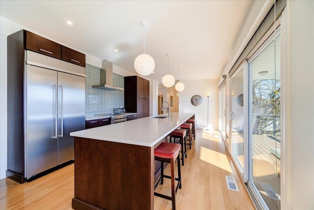 kitchen with a kitchen breakfast bar, wall chimney exhaust hood, decorative backsplash, appliances with stainless steel finishes, and decorative light fixtures