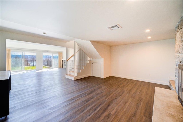 unfurnished living room with a stone fireplace and dark wood-type flooring