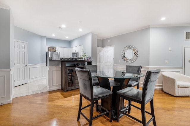 dining space featuring ornamental molding, beverage cooler, and light hardwood / wood-style floors