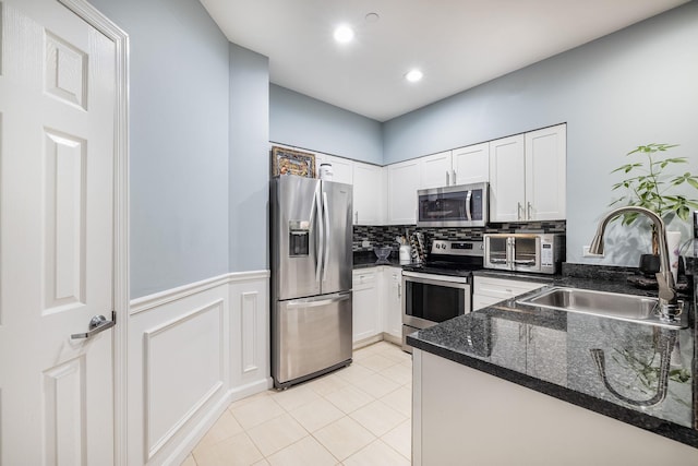 kitchen featuring sink, light tile patterned floors, appliances with stainless steel finishes, white cabinets, and dark stone counters