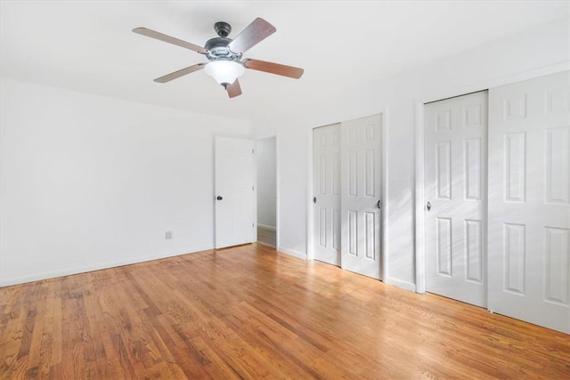 unfurnished bedroom with ceiling fan, light wood-type flooring, and multiple closets