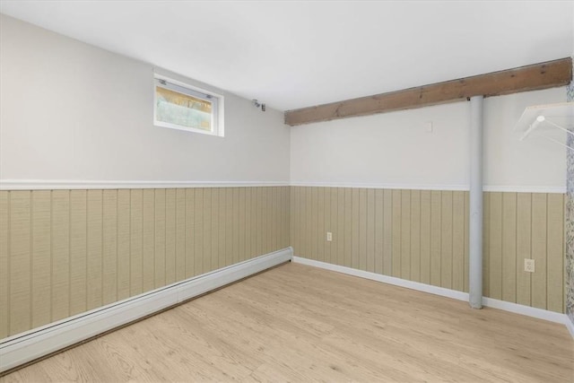 basement with light wood-type flooring, baseboard heating, and wooden walls