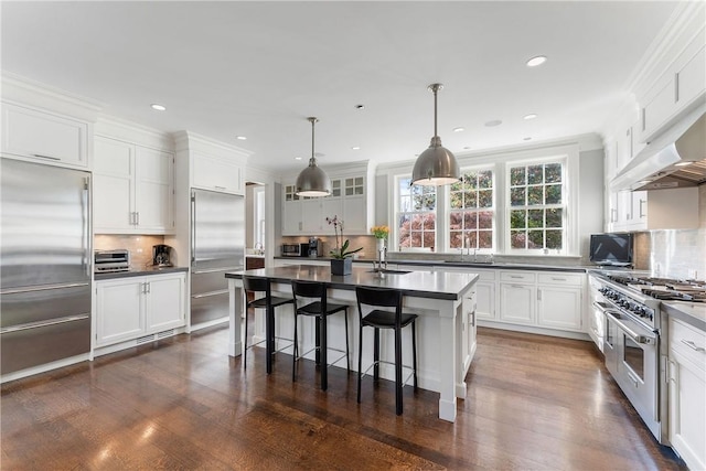 kitchen featuring backsplash, a kitchen island with sink, hanging light fixtures, premium appliances, and white cabinetry