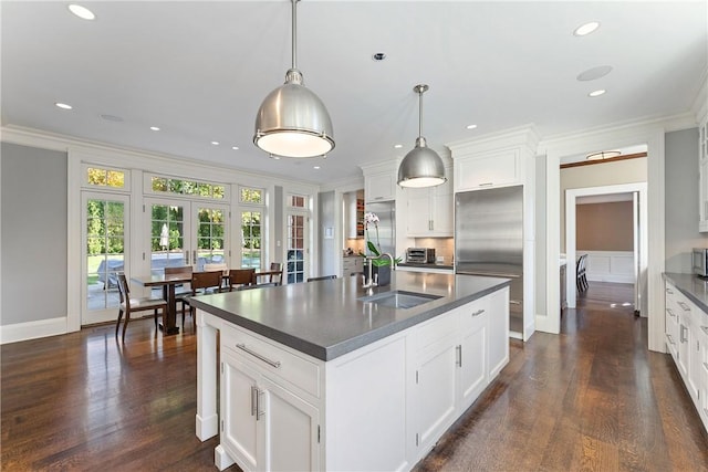 kitchen featuring sink, hanging light fixtures, a center island with sink, white cabinets, and ornamental molding