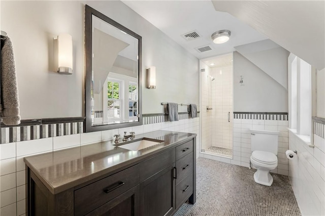 bathroom with tile patterned flooring, toilet, vanity, a shower with shower door, and tile walls