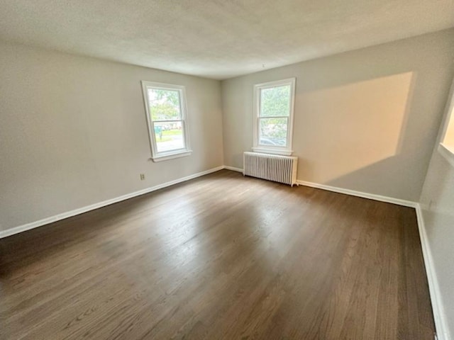 empty room with dark hardwood / wood-style flooring and radiator