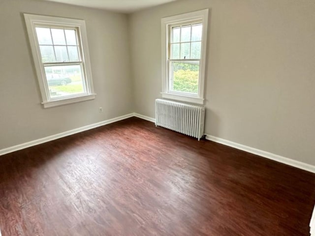 unfurnished room featuring a wealth of natural light, dark hardwood / wood-style floors, and radiator