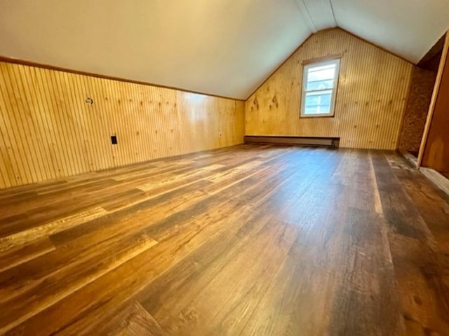 additional living space with hardwood / wood-style floors, wood walls, baseboard heating, and vaulted ceiling