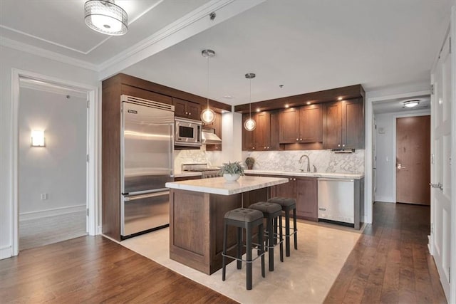 kitchen featuring pendant lighting, a center island, backsplash, light hardwood / wood-style flooring, and built in appliances