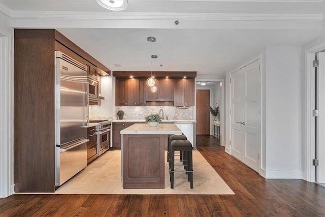 kitchen with built in appliances, pendant lighting, light hardwood / wood-style floors, decorative backsplash, and a kitchen island