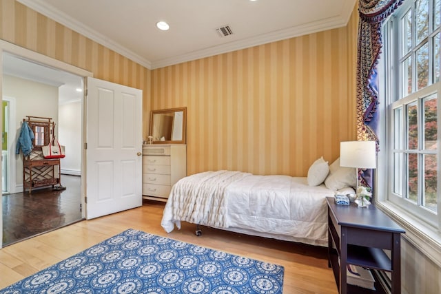 bedroom with wallpapered walls, crown molding, visible vents, and wood finished floors