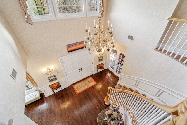 entrance foyer with visible vents, a towering ceiling, a wainscoted wall, stairs, and a decorative wall