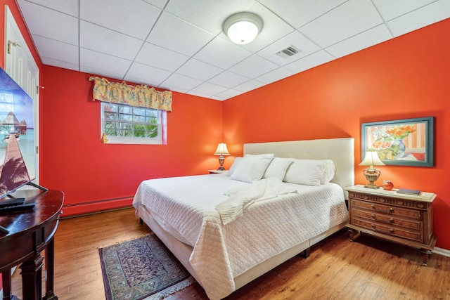 bedroom with a baseboard radiator, a paneled ceiling, wood finished floors, visible vents, and baseboards