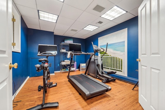 workout area featuring a paneled ceiling, wood finished floors, visible vents, and baseboards