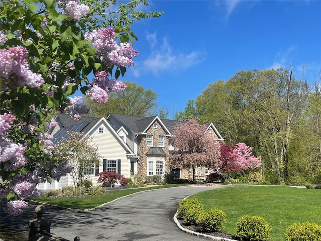 view of front of house with stone siding, a front yard, and driveway