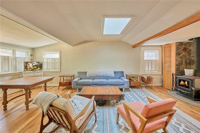 living room featuring vaulted ceiling with skylight, a healthy amount of sunlight, light wood-type flooring, and a wood stove