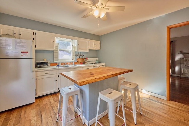 kitchen featuring white appliances, wooden counters, light hardwood / wood-style floors, white cabinetry, and a breakfast bar area