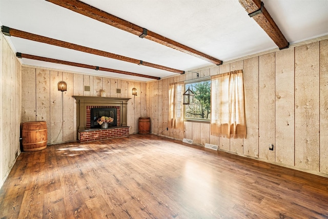 unfurnished living room featuring beam ceiling, wood walls, wood-type flooring, and a brick fireplace