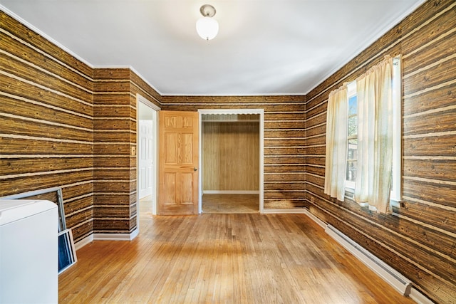 spare room featuring washer / dryer, wood walls, a baseboard heating unit, and hardwood / wood-style flooring