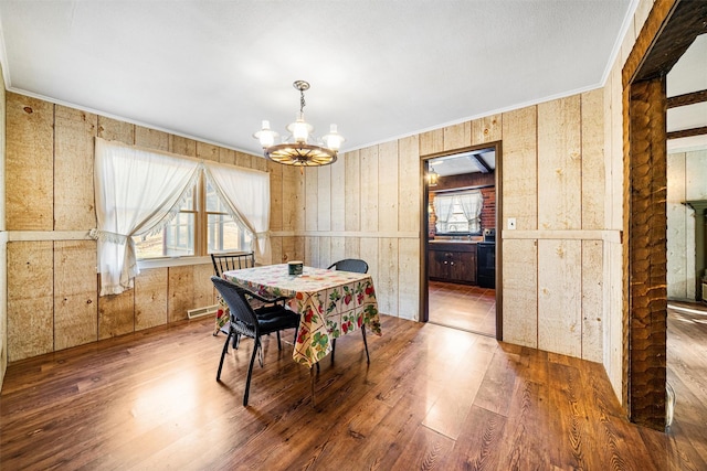 dining area featuring hardwood / wood-style floors, crown molding, a notable chandelier, and wood walls