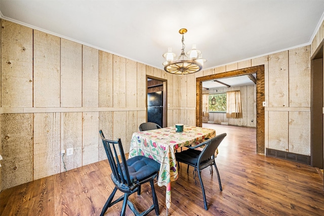 dining room with a chandelier, hardwood / wood-style floors, crown molding, and wood walls