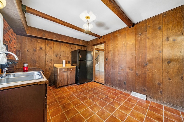 kitchen with beam ceiling, sink, black fridge, tile patterned floors, and wood walls