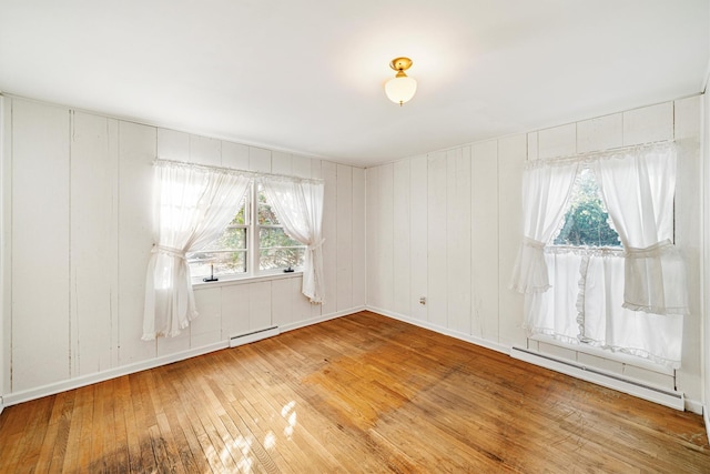 spare room with baseboard heating, wood walls, and hardwood / wood-style floors