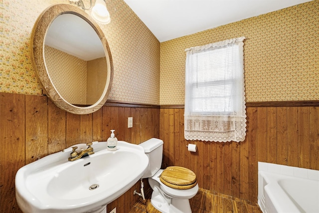 bathroom featuring wood walls, sink, a bath, and toilet