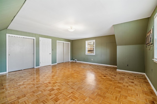 unfurnished bedroom featuring light parquet floors, lofted ceiling, wooden walls, and multiple closets