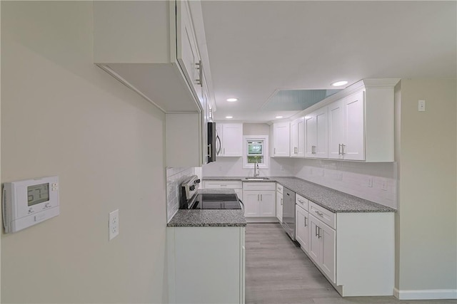 kitchen featuring sink, dark stone countertops, appliances with stainless steel finishes, light hardwood / wood-style floors, and white cabinetry