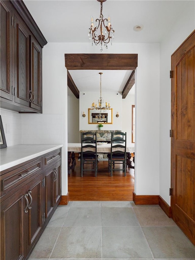 interior space with an inviting chandelier, hanging light fixtures, tasteful backsplash, dark brown cabinetry, and beamed ceiling