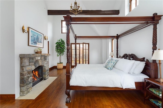 bedroom featuring dark hardwood / wood-style flooring, a stone fireplace, and lofted ceiling with beams