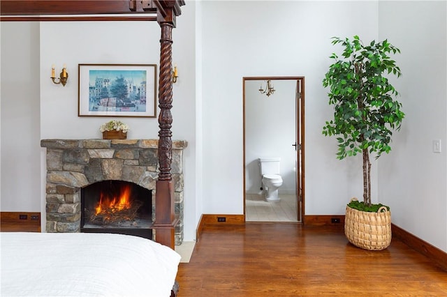 bedroom featuring hardwood / wood-style flooring, a stone fireplace, and ensuite bathroom