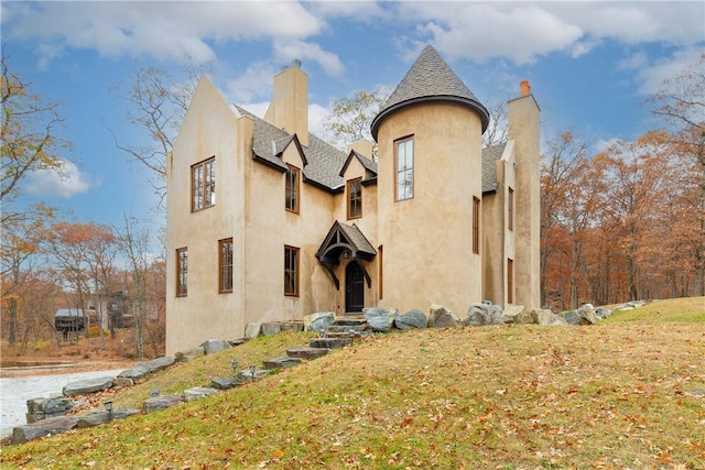 view of front facade with stucco siding, a front lawn, roof with shingles, and a chimney