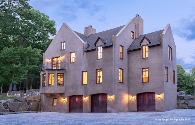 view of front of property featuring stucco siding, driveway, a balcony, and a chimney