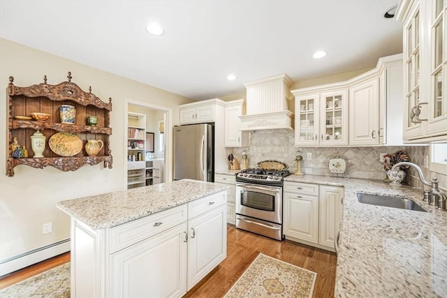 kitchen with premium range hood, stainless steel appliances, sink, a baseboard radiator, and white cabinetry