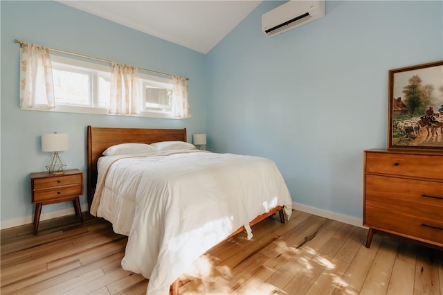 bedroom with vaulted ceiling, light hardwood / wood-style floors, and a wall mounted air conditioner