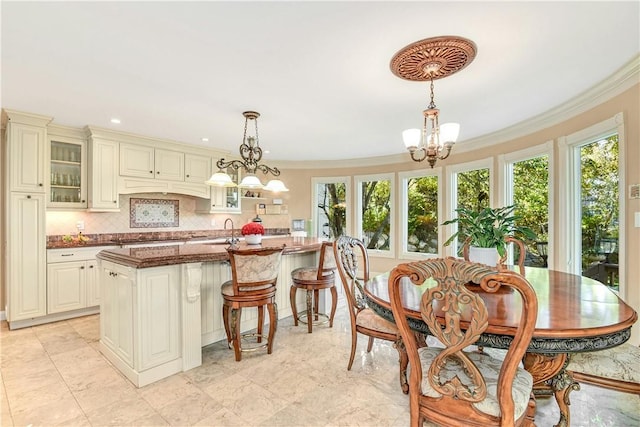 kitchen with ornamental molding, sink, decorative light fixtures, a chandelier, and an island with sink