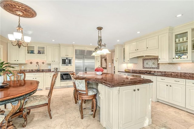 kitchen featuring an inviting chandelier, built in appliances, dark stone countertops, pendant lighting, and a kitchen island