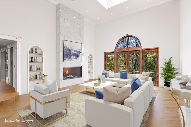 living room featuring a large fireplace, built in features, light parquet floors, a towering ceiling, and ornamental molding