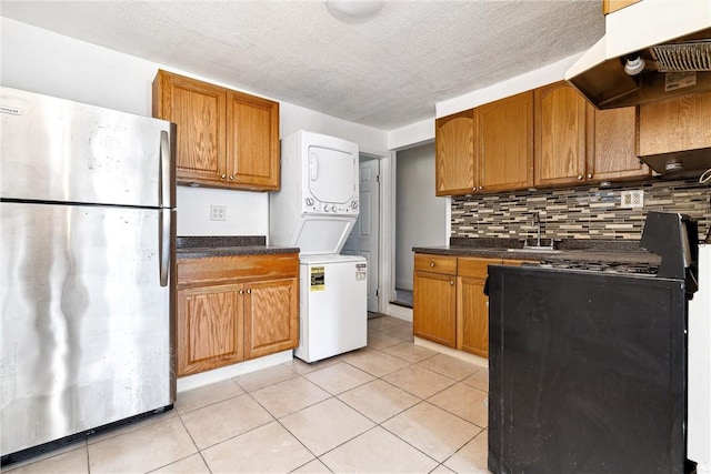 kitchen featuring sink, range hood, stacked washer / drying machine, light tile patterned flooring, and stainless steel refrigerator