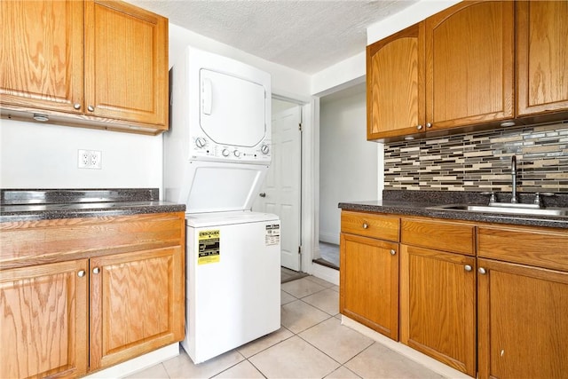 laundry area with light tile patterned floors, a textured ceiling, stacked washer / dryer, and sink