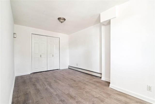 unfurnished bedroom with baseboard heating, a closet, and light hardwood / wood-style flooring