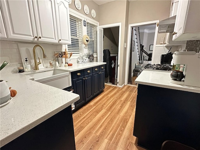 kitchen featuring decorative backsplash, sink, stainless steel range oven, white cabinets, and light hardwood / wood-style floors