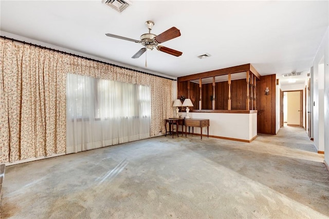 unfurnished living room featuring ceiling fan, wood walls, and light carpet