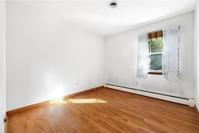 unfurnished room featuring baseboard heating and hardwood / wood-style floors