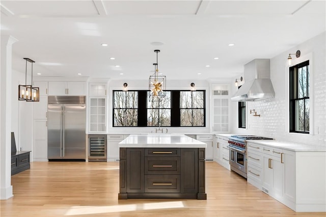 kitchen featuring island exhaust hood, beverage cooler, pendant lighting, high quality appliances, and white cabinets