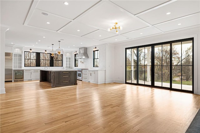 unfurnished living room featuring coffered ceiling, beverage cooler, light hardwood / wood-style flooring, and a notable chandelier